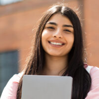 confident college student holding a laptop showing how mental health tips can be helpful for college students.
